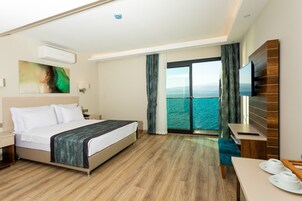 Habitación de hotel con cama, escritorio, televisor y vista al mar.