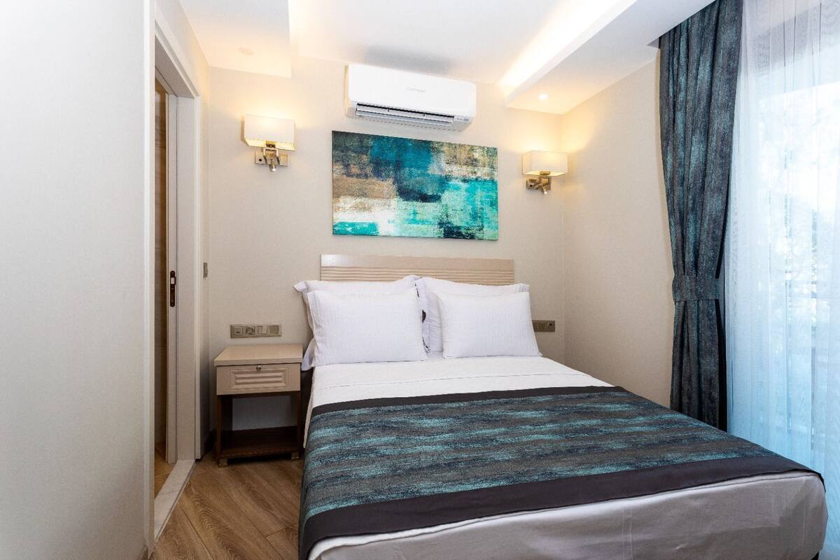 Een hotelkamer met een bed, nachtkastjes, een airconditioning en een schilderij aan de muur.