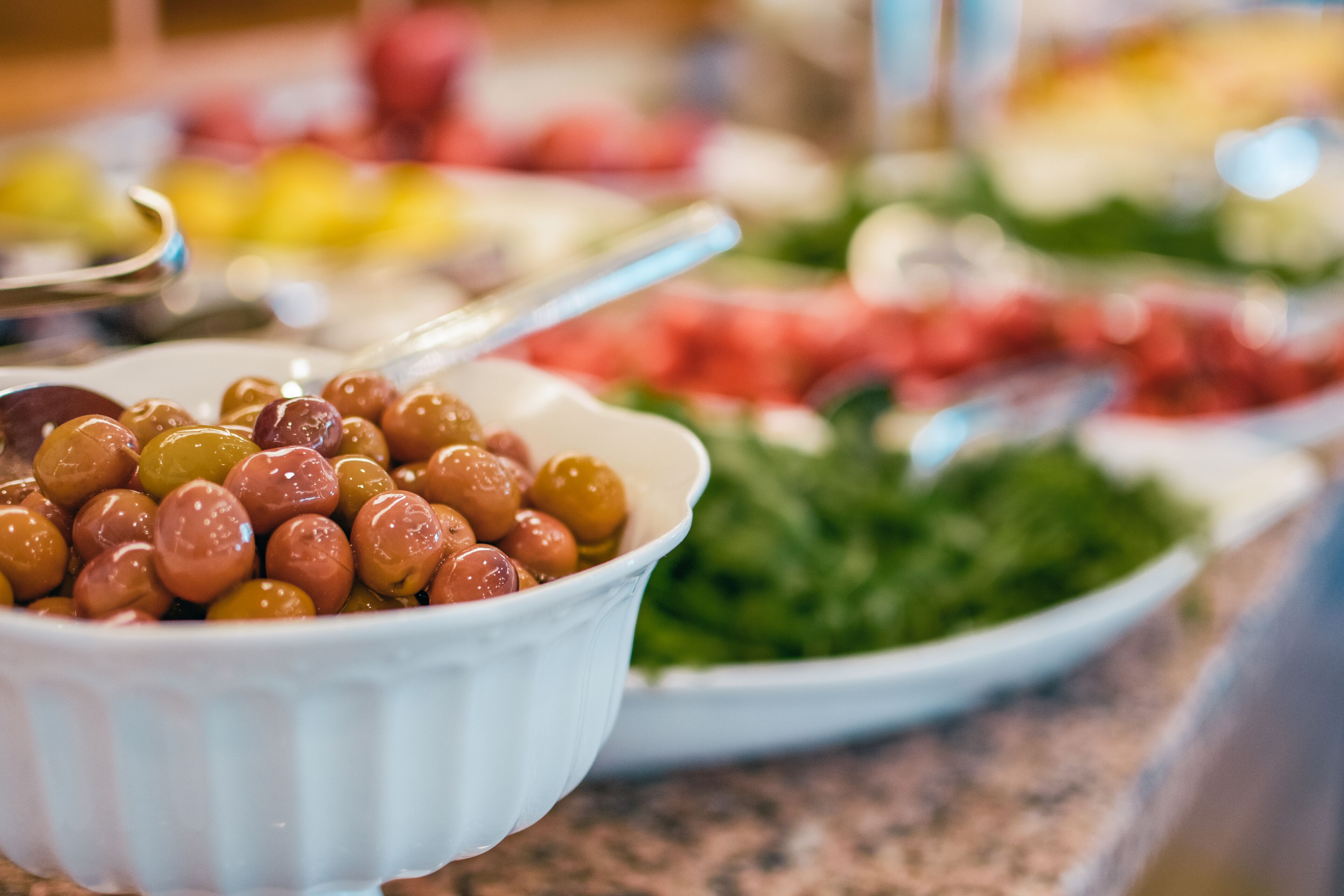 Un bufé con diversos platos, incluyendo un bol de aceitunas y una bandeja de verduras.