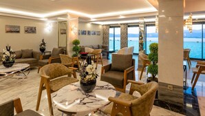 Een moderne woonkamer met een marmeren salontafel, comfortabele zithoeken en een groot raam met uitzicht op zee.
