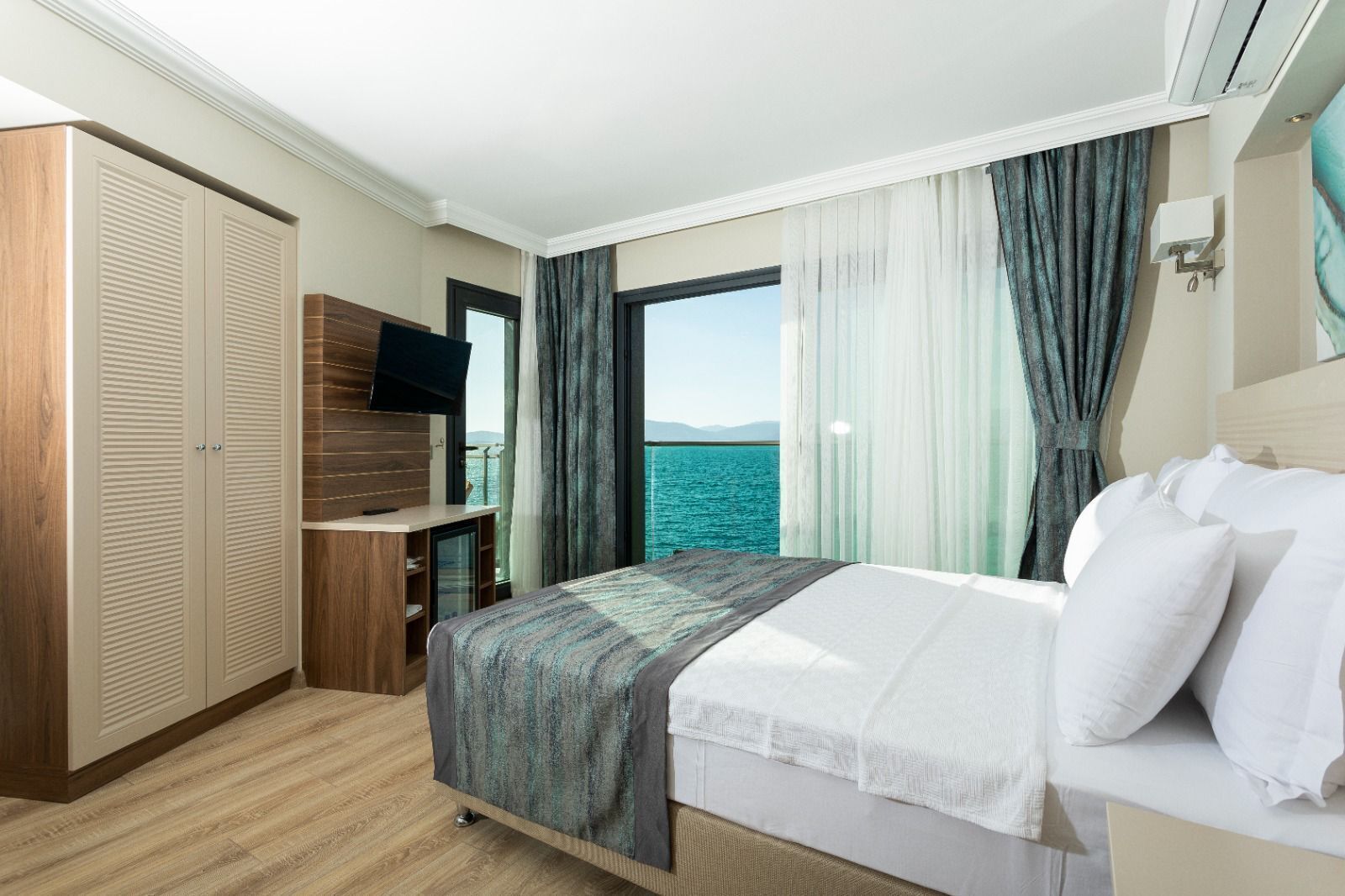 Ein Hotelzimmer mit Bett, Fernseher, Kleiderschrank und Meerblick.