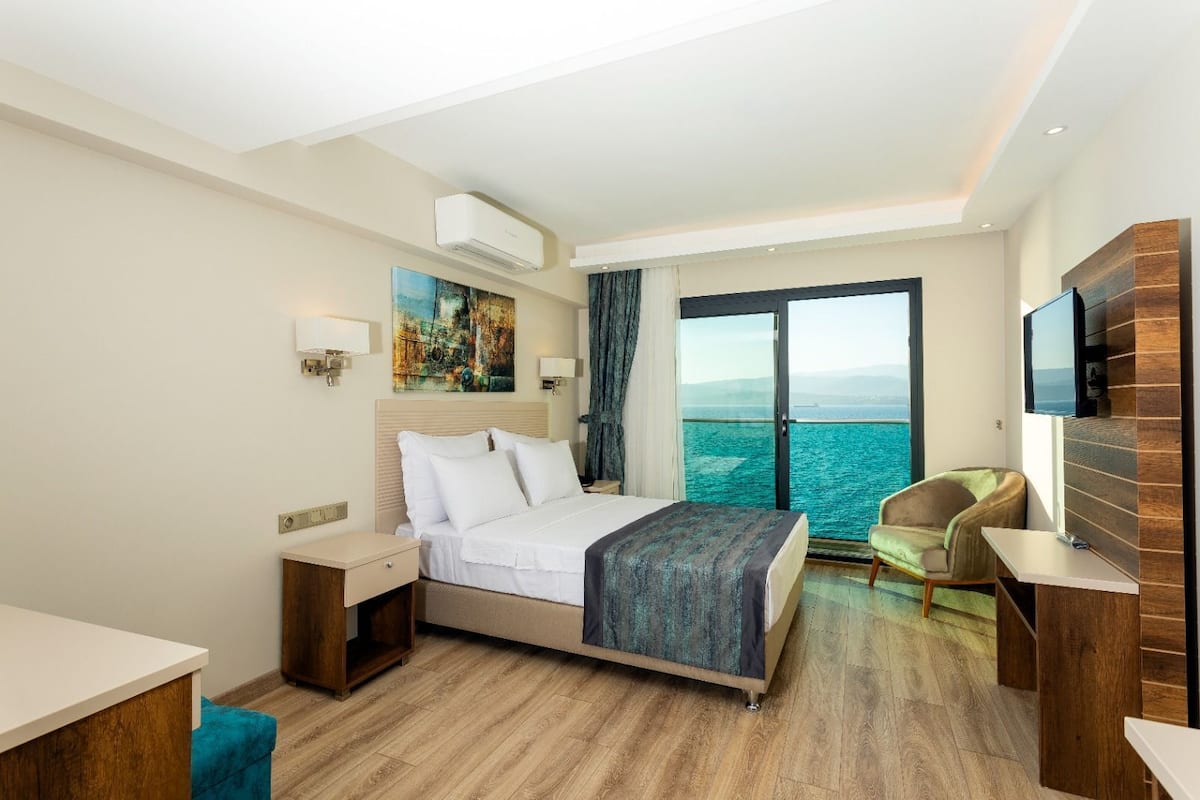 Een moderne hotelkamer met een bed, een bureau, een stoel en een groot raam met uitzicht op zee.