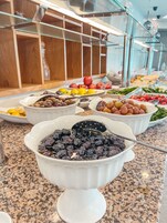 Un bufé con diversas opciones de comida, incluyendo frutas, verduras y un tazón de aceitunas negras.
