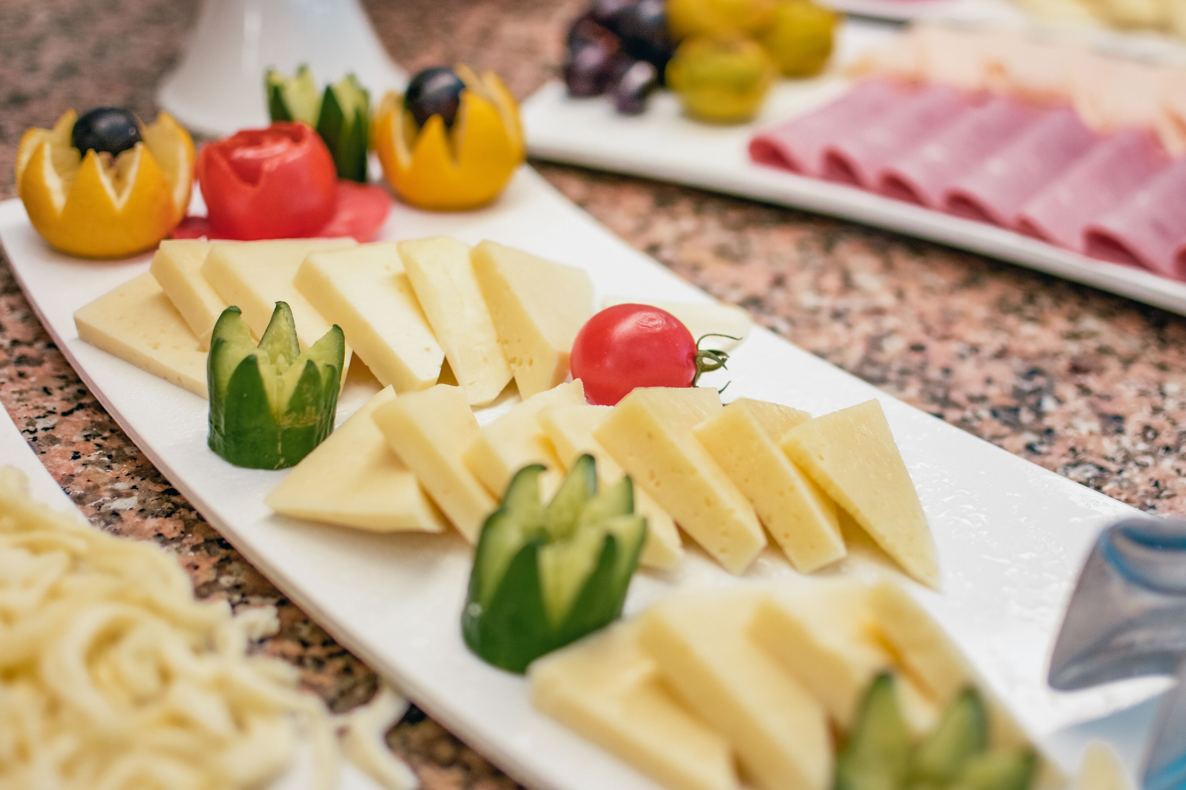 A cheese board with various cheeses and vegetables on a white plate.