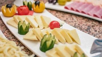 A cheese board with various cheeses and vegetables on a white plate.