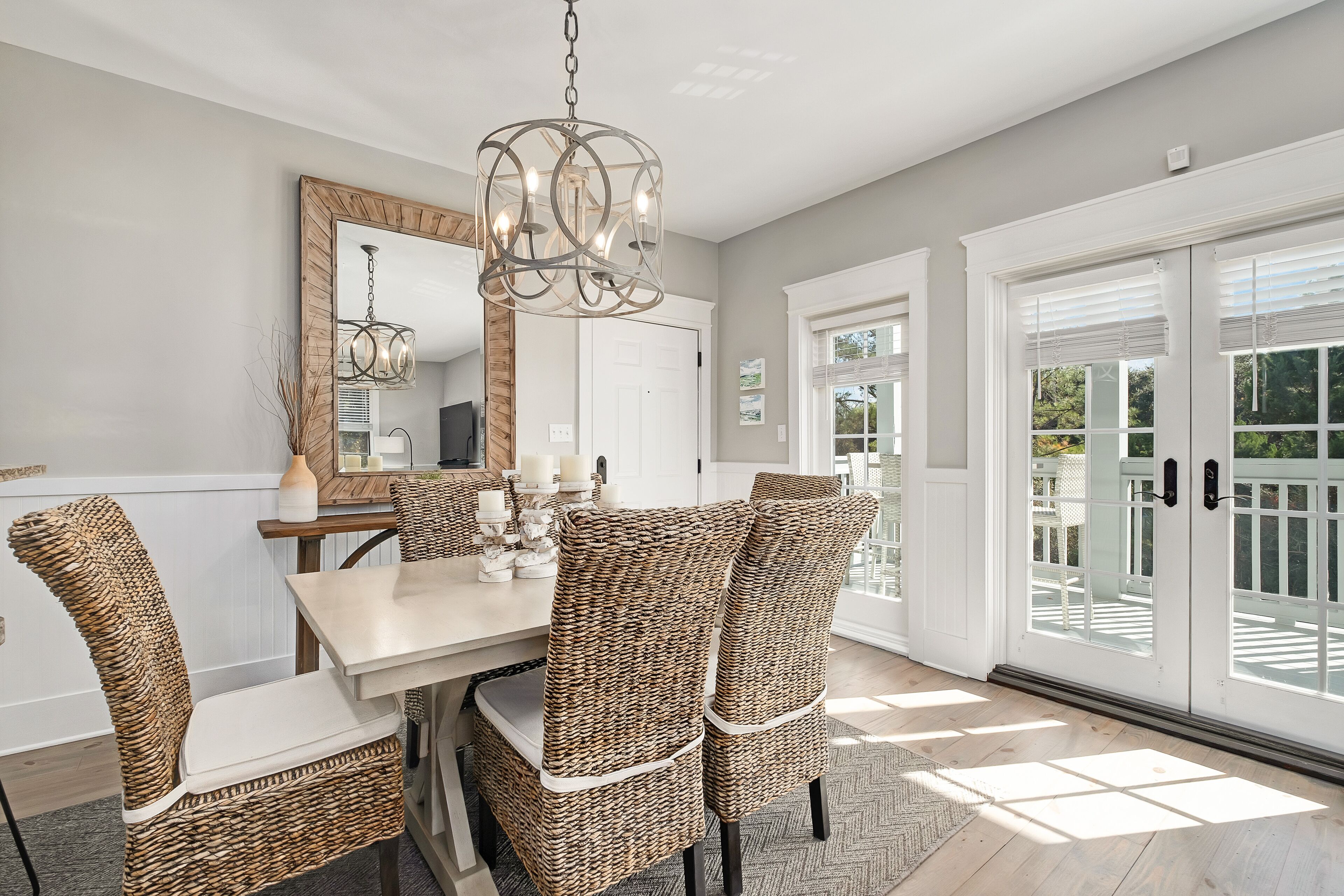 A dining area with wicker chairs, a white table, and a chandelier.