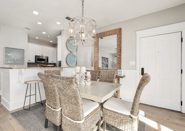 A modern kitchen with white cabinets, a built-in oven, and a dining area with wicker chairs and a light-colored table.