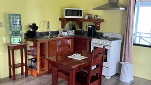 A compact kitchen with a dining area, a water dispenser, a microwave, a stove, and a window with curtains. - Tranquil romantic getaway (Belize)