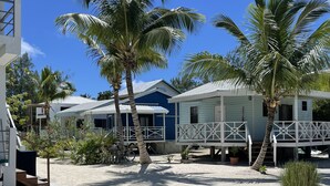 A beachfront property with two houses, one with a blue exterior and the other with a light blue exterior. Both houses have white railings and are elevated on stilts. There is a sign indicating 'BARRACUDA COTTAGE' on the light blue house. - Tranquil romantic getaway (Belize)