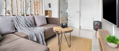 Een moderne woonkamer met een bank, een ronde houten salontafel en een aan de muur bevestigde televisie.