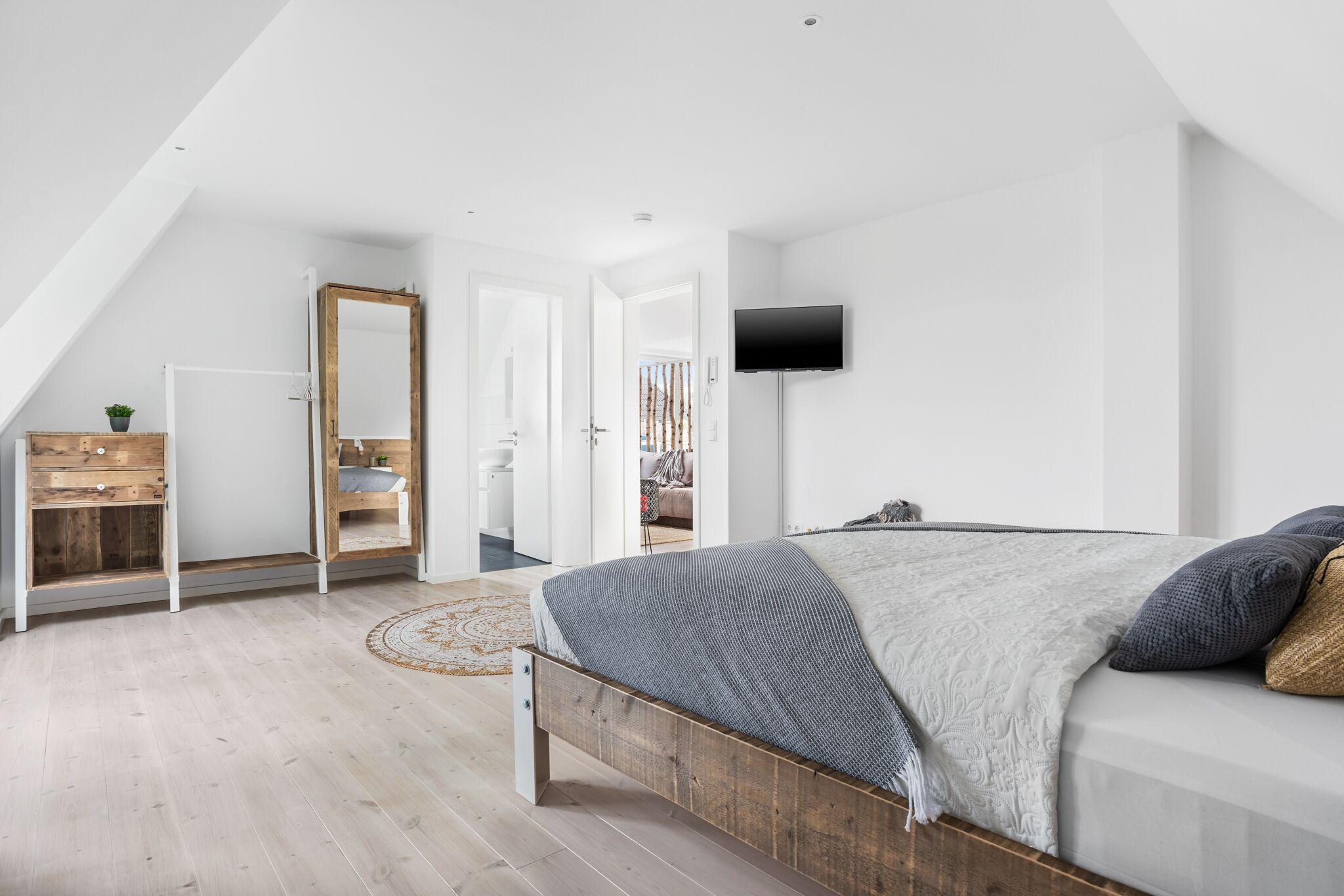 Een moderne slaapkamer met een houten bed, een flatscreen televisie en een grote spiegel.