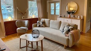 A cozy living room with a sofa, two armchairs, a coffee table, and a large window with curtains.