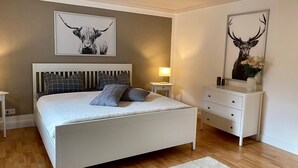 A bedroom with a white bed, grey and black pillows, a bedside table, a nightstand, a lamp, and two wall-mounted artworks of animals.