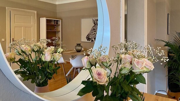A room with a large mirror reflecting a dining area, a white door, and a bookshelf.