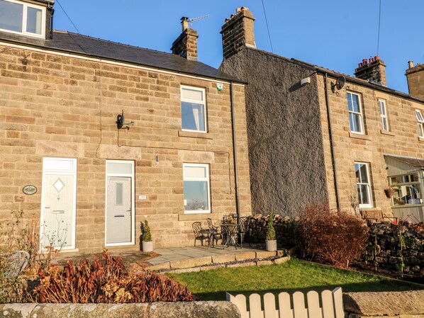 A two-story stone house with a front door, a small garden, and a paved patio area. - Cavendish Cottage (Matlock)