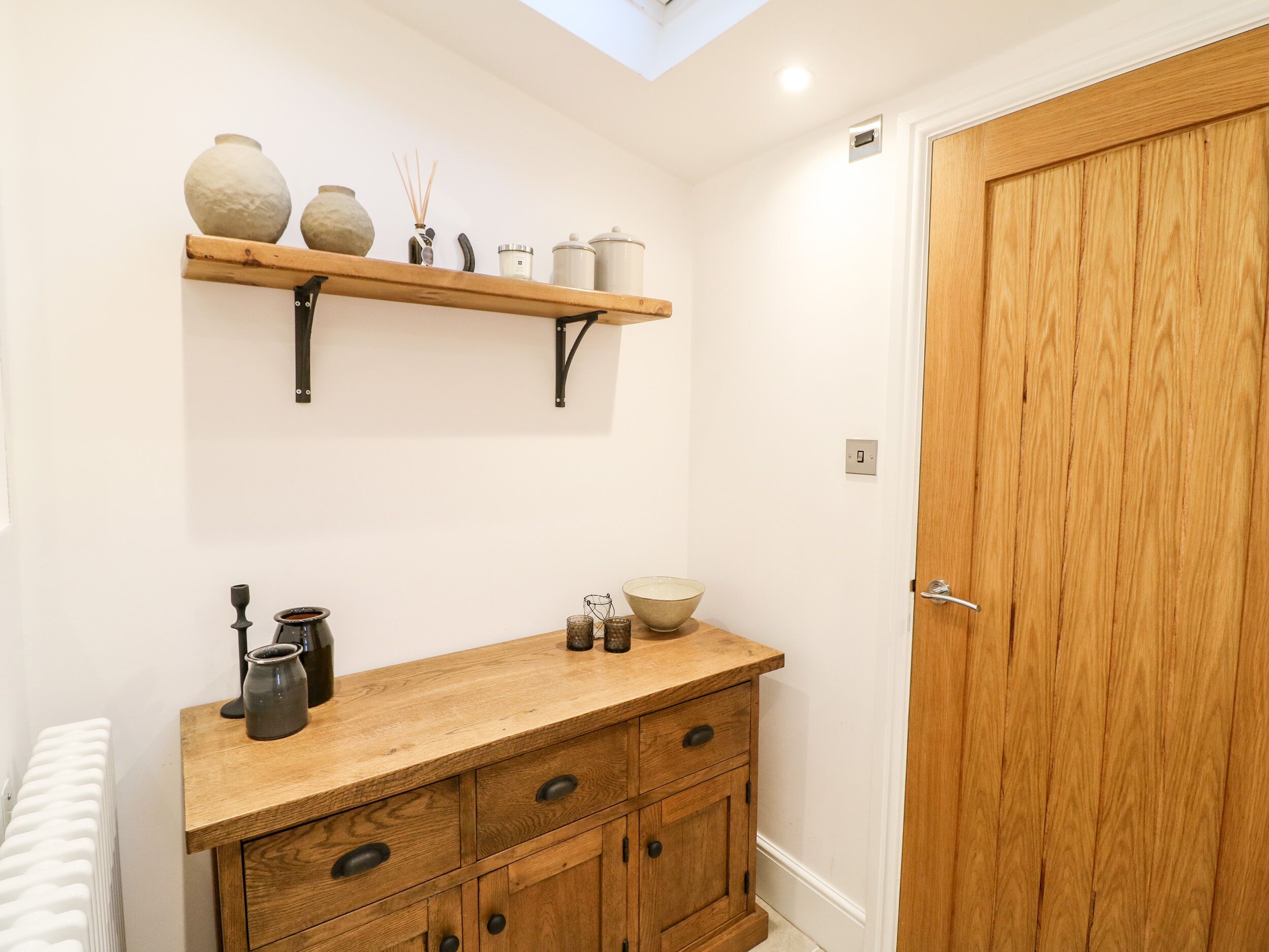 Een badkamer met een houten wastafelmeubel, een plank met decoratieve spullen, en een houten deur.