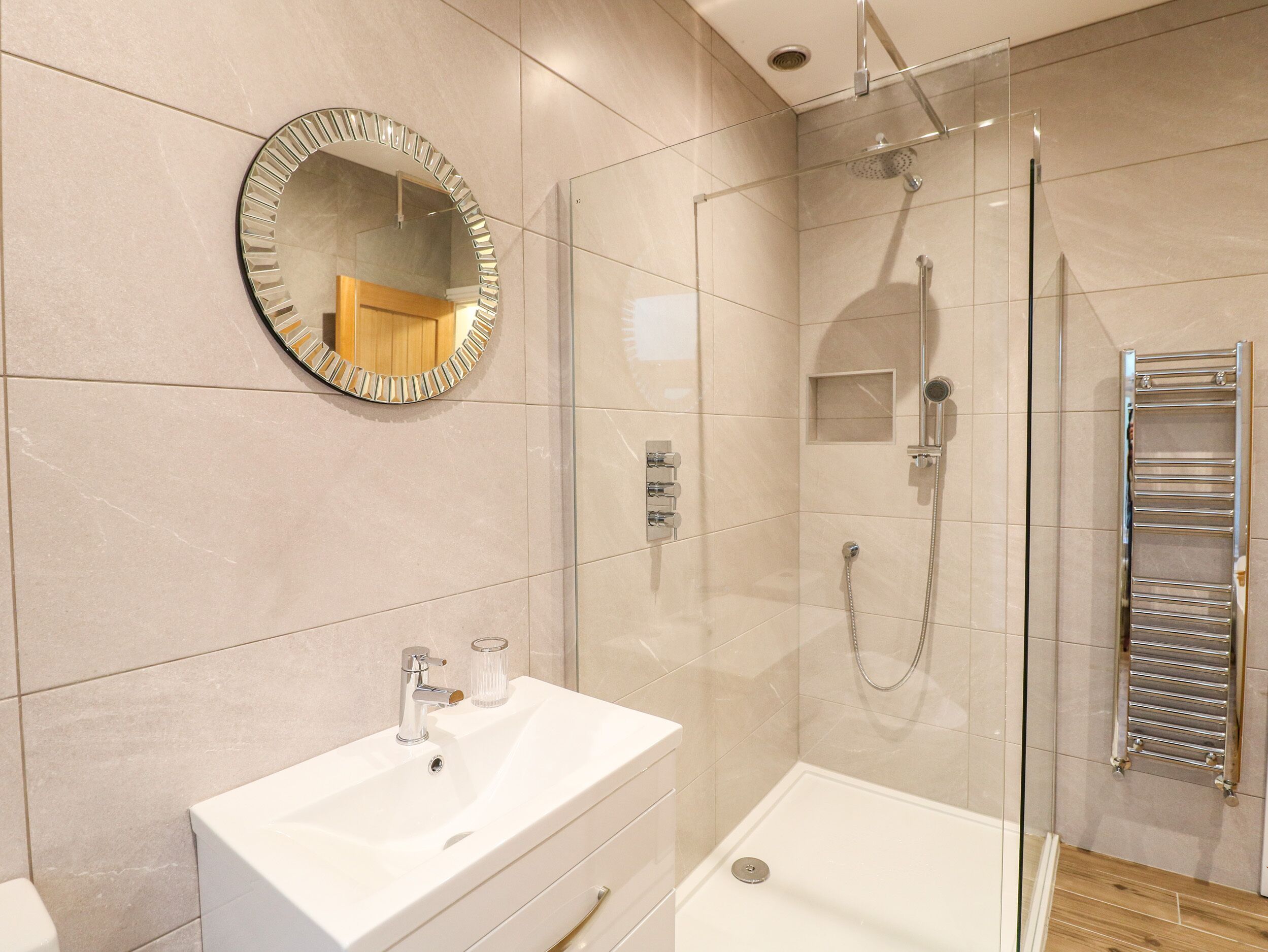 A modern bathroom with a glass-enclosed shower, a white sink, and a round mirror.