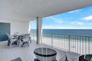Een balkon met uitzicht op de oceaan, een eettafel met stoelen en een afvalbak.