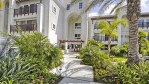 A multi-story building with balconies, a central courtyard with palm trees, and a pathway leading to the entrance. - Condo on property at LaCosta Golf Resort & Spa 689 (Carlsbad)