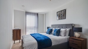 A modern bedroom with a large bed, a nightstand, a wall-mounted lamp, and a geometric art piece. - Modern 2 Bedroom Riverside Apartment in Leeds (Leeds)