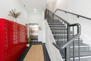 A staircase with metal railings, a red storage unit, and a potted plant. - Stylish & Spacious 1-Bed Flat in a Converted Mill (Leeds)