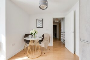 A modern dining area with a round table, two chairs, and a vase of flowers. - Stylish & Spacious 1-Bed Flat in a Converted Mill (Leeds)