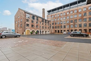 A multi-story building with brick facade, large windows, and a parking area with cars.