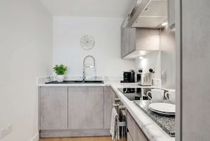 A modern kitchen with a sink, countertop, and a clock on the wall.