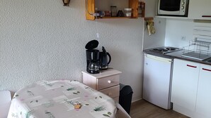 Une cuisine compacte équipée d’une machine à café, d’un four à micro-ondes et d’un évier. On y trouve une table recouverte d’une nappe à motifs floraux et une chaise.