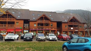 Une rangée de bâtiments en bois dotés de nombreux balcons, une zone centrale réservée aux piétons et plusieurs voitures garées.