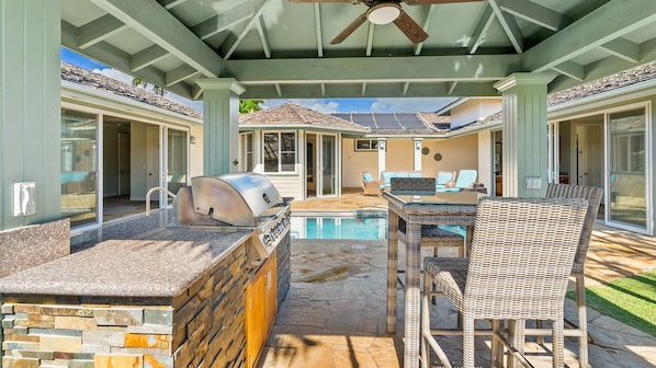 An outdoor patio with a stone countertop, grill, and wicker chairs.