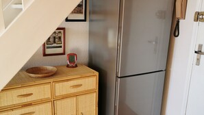 Una cocina con un refrigerador de acero inoxidable, armarios de madera, una mesa de comedor de madera con un tazón, y una escalera que lleva a un nivel superior.