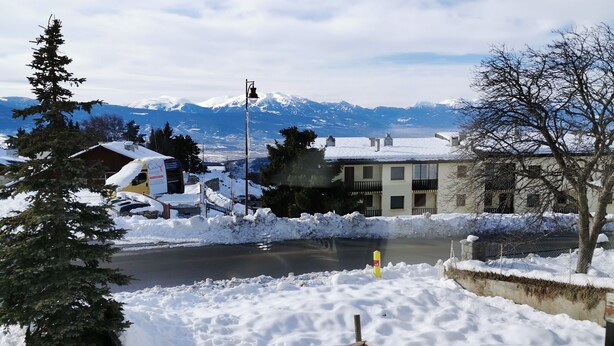 Paisaje nevado con una montaña al fondo, una carretera y edificios.