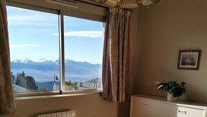 Un dormitorio con una cama grande, un radiador, una ventana con cortinas, una planta y un cuadro en la pared.