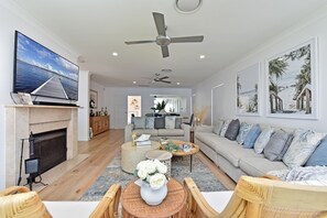 A modern living room with a flat-screen TV, a fireplace, a sofa set, and a dining area with a coffee table. - Reflections at Sunset Beach (Soldiers Point)