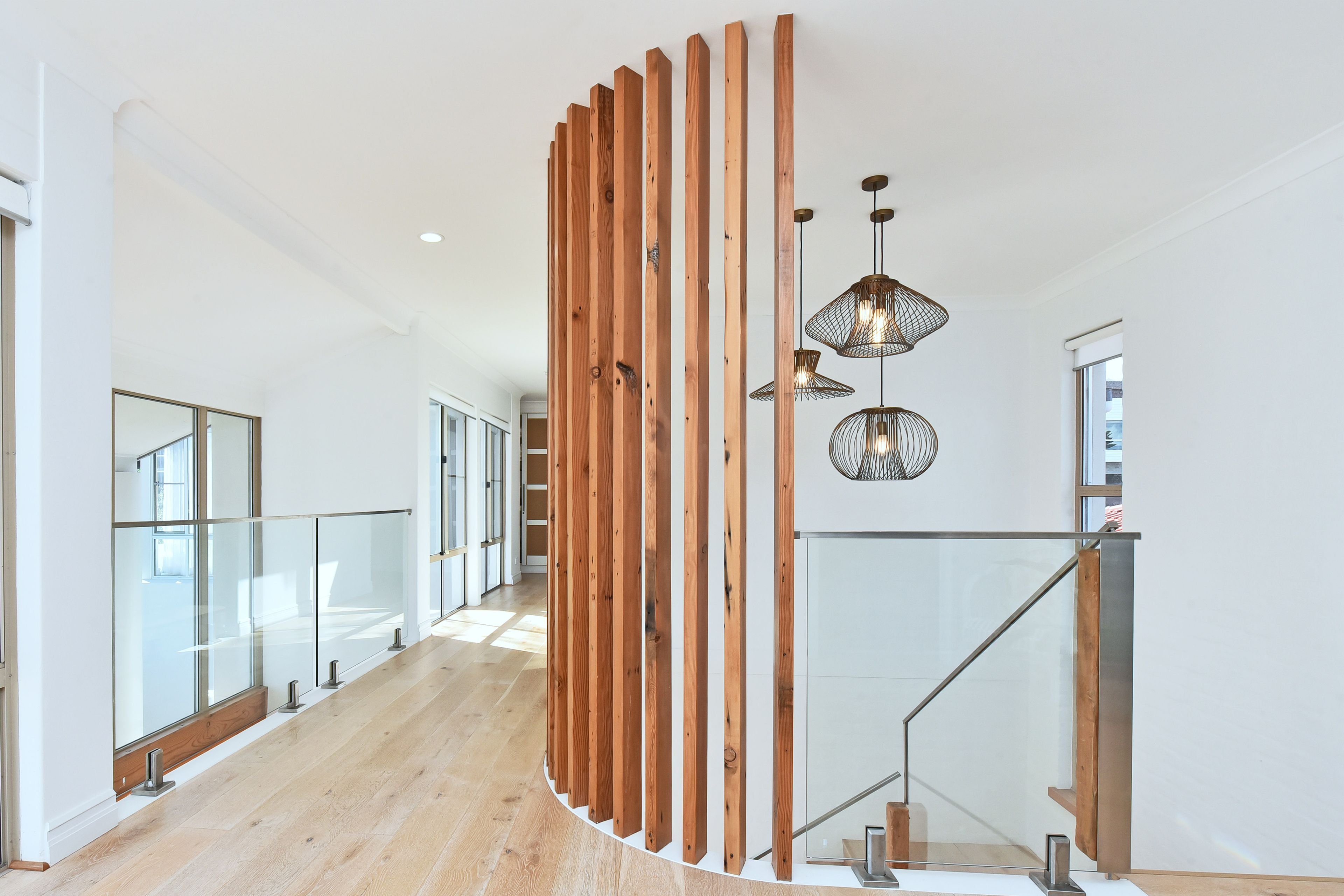 Un intérieur moderne avec un séparateur en bois aux lignes courbes, des rampes en verre et des luminaires suspendus.