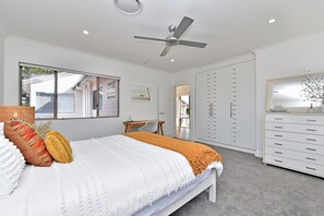 A bedroom with a bed, a ceiling fan, a desk, and a wardrobe. - Reflections at Sunset Beach (Soldiers Point)