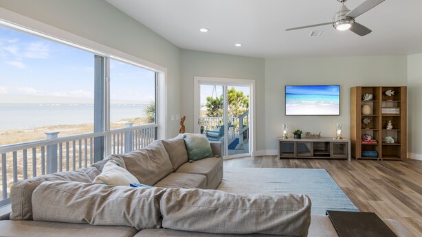 A spacious living room with a large sectional sofa, a wooden floor, a ceiling fan, and a large window overlooking a beach. - Casa Caribe-Soundside Private Home w/Pool and Tennis 2 Min from the Beach (Navarre)