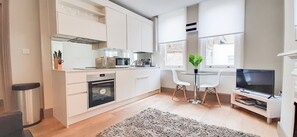 A modern kitchen with white cabinets, a microwave, oven, and a dining area with a table and chairs. - Beautiful 1-bed Apartment in Central London (London)