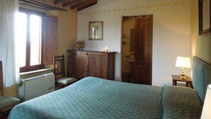 A bedroom with a bed, a dresser, a chair, a window, and a door. - Villa Cenerentola (Trequanda)