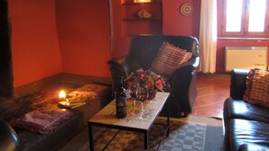 A cozy living room with a fireplace, a black leather sofa, a table with a vase of flowers, and a window with curtains. - Villa Cenerentola (Trequanda)