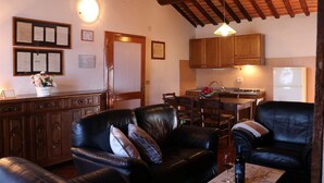 A cozy living room with a fireplace, a dining area, and a kitchen with wooden cabinets. - Villa Cenerentola (Trequanda)