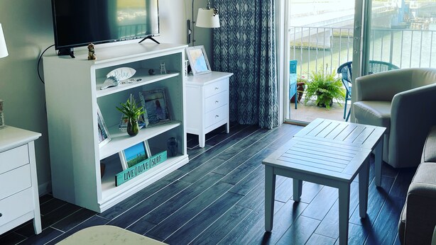 A modern living room with a flat-screen TV, a white cabinet with shelves, a small table, a sofa, and a view of a bridge through a large window.