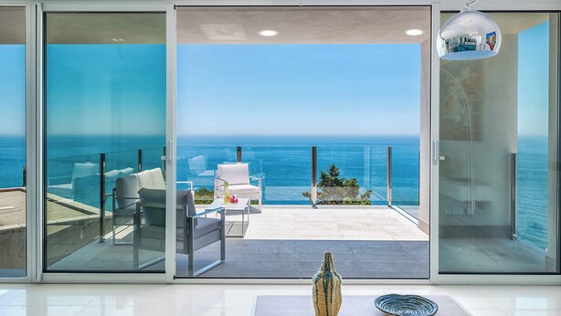 Ein moderner Balkon mit Glastür, weißer Möbel und Blick aufs Meer.