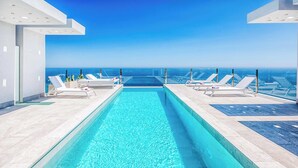 Ein moderner Infinity-Pool mit klarem, blauem Wasser, umgeben von Liegestühlen und Blick auf den Ozean.