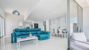 Ein modernes Wohnzimmer mit einem türkisfarbenen Sofa, einem weißen Couchtisch und einer Glastrennwand.