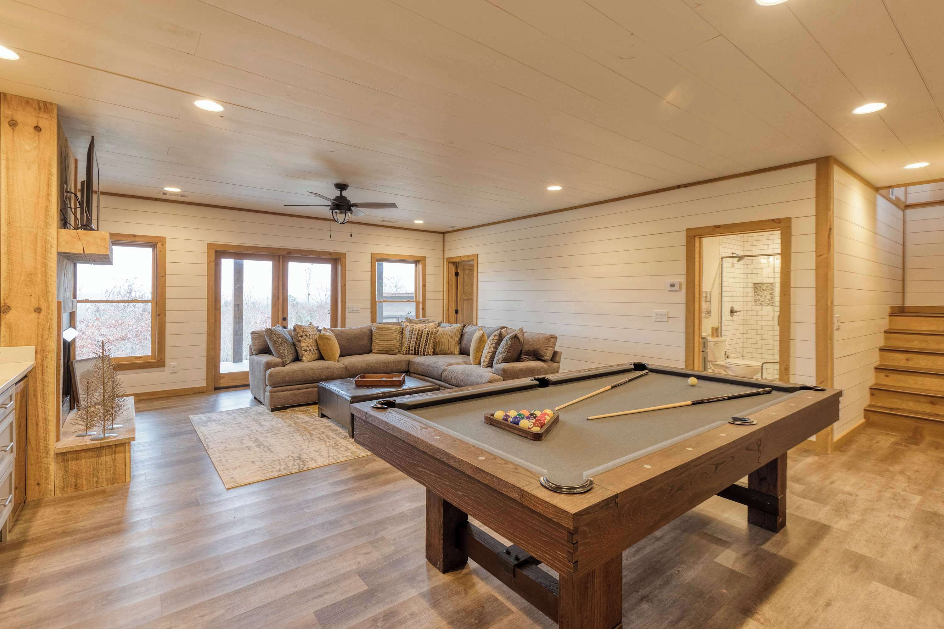 A pool table in a room with wooden flooring, a sofa, and a ceiling fan.