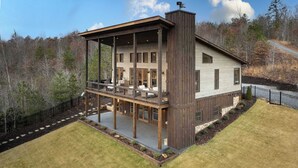 Een houten huis met twee verdiepingen, een balkon, een overdekte patio en uitzicht op een bebost gebied.