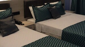 Habitación de hotel con dos camas, cada una con una colcha verde estampada. En la pared, sobre las camas, hay una obra de arte floral grande.
