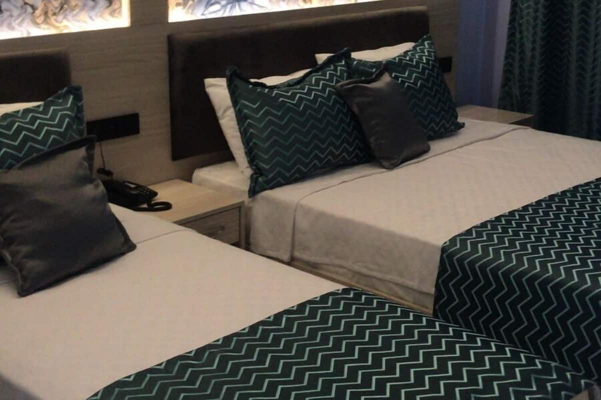 A hotel room with two beds, each with a green patterned bedspread. There is a large floral artwork on the wall above the beds.